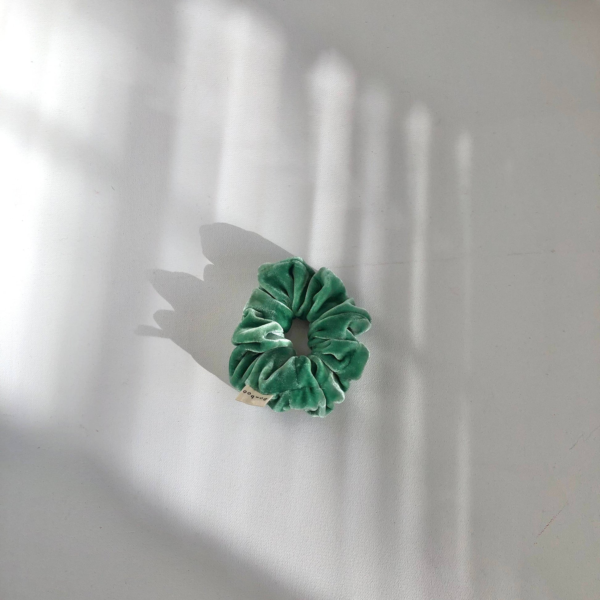Green scrunchie on a white surface with shadows