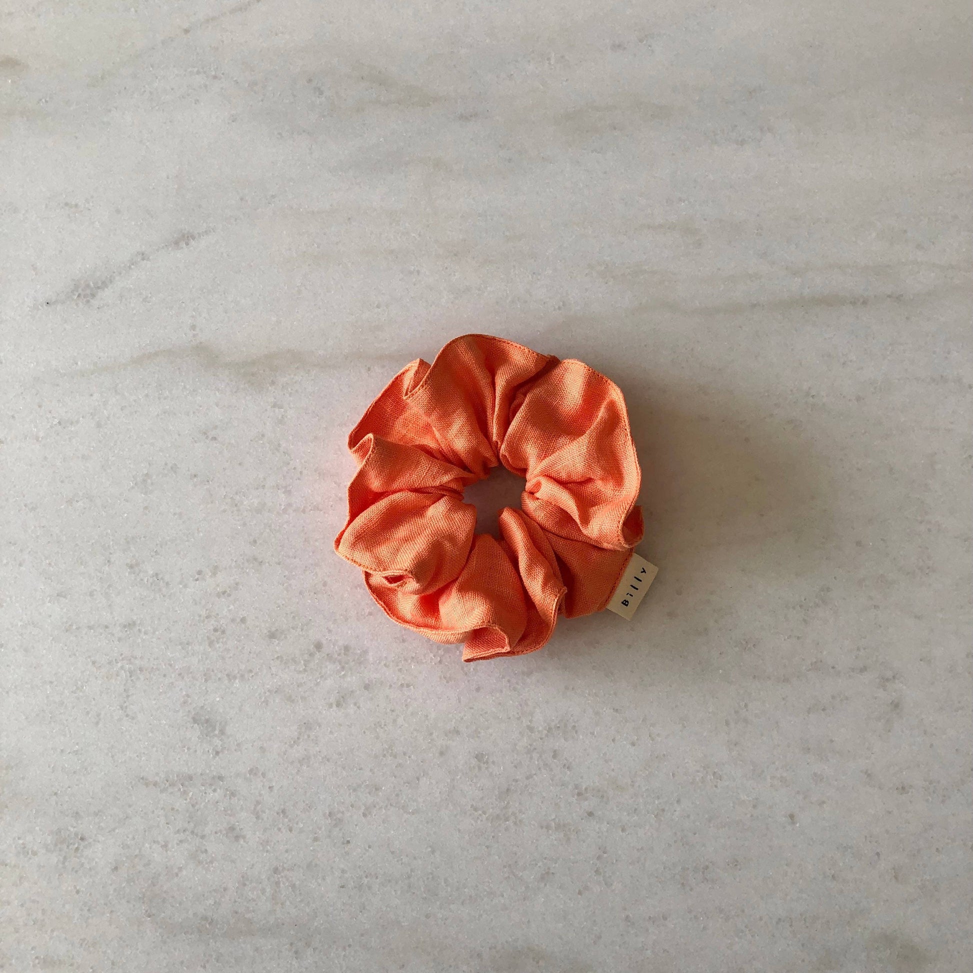 Orange scrunchie on a light gray marble surface