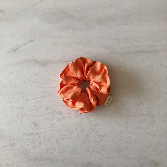 Orange scrunchie on a light gray marble surface