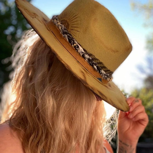 Blond haired woman wears a hand made tan wool hat with a sun burned on it covering her face